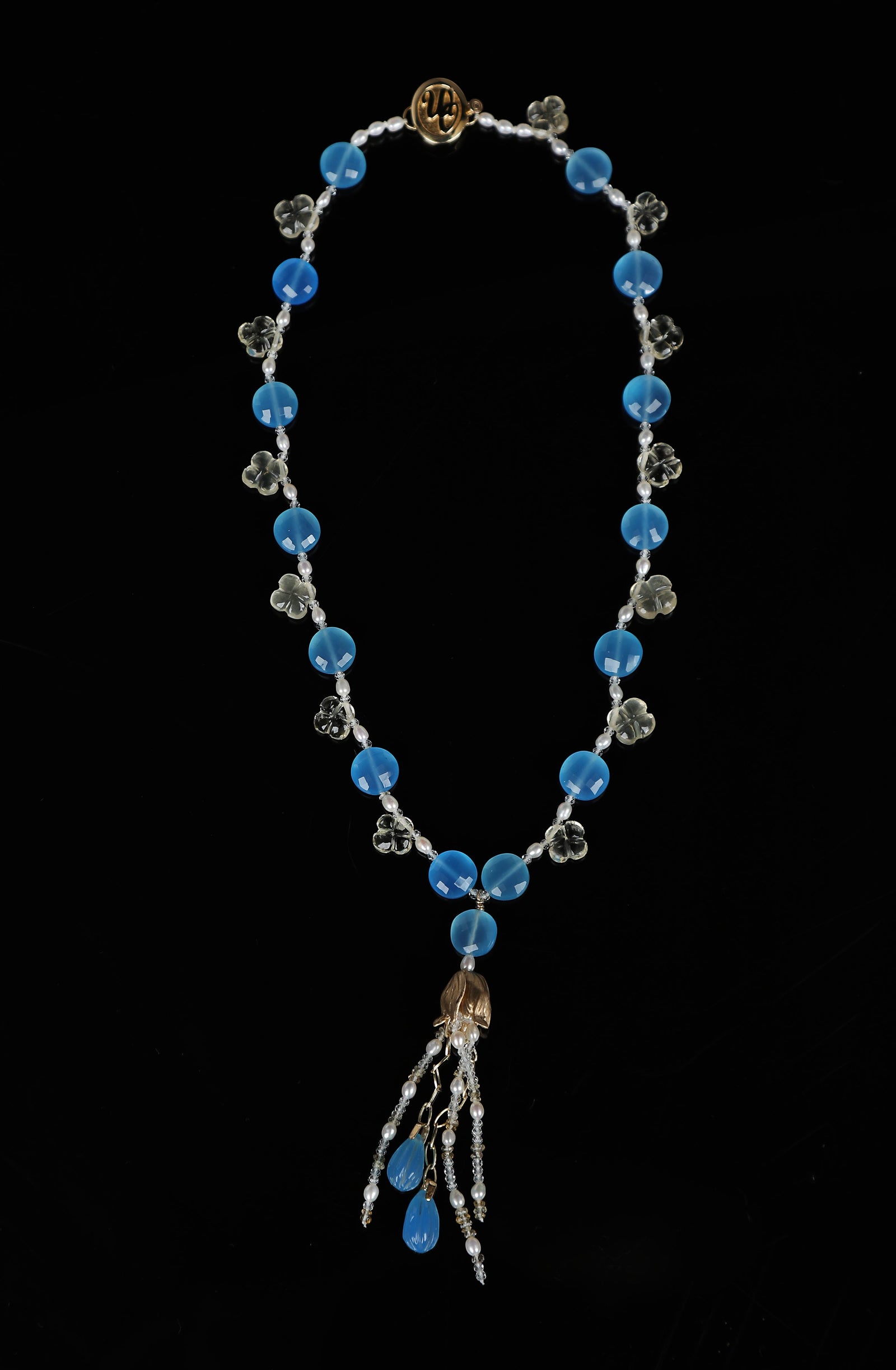 14kt yellow gold choker necklace (16”) with a tassel (3”). Gems: blue chalcedony, carved scapolite, white topaz, and pearl.