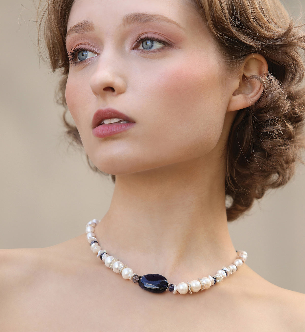 Woman wearing a pearl necklace with a dark stone on a neutral background
