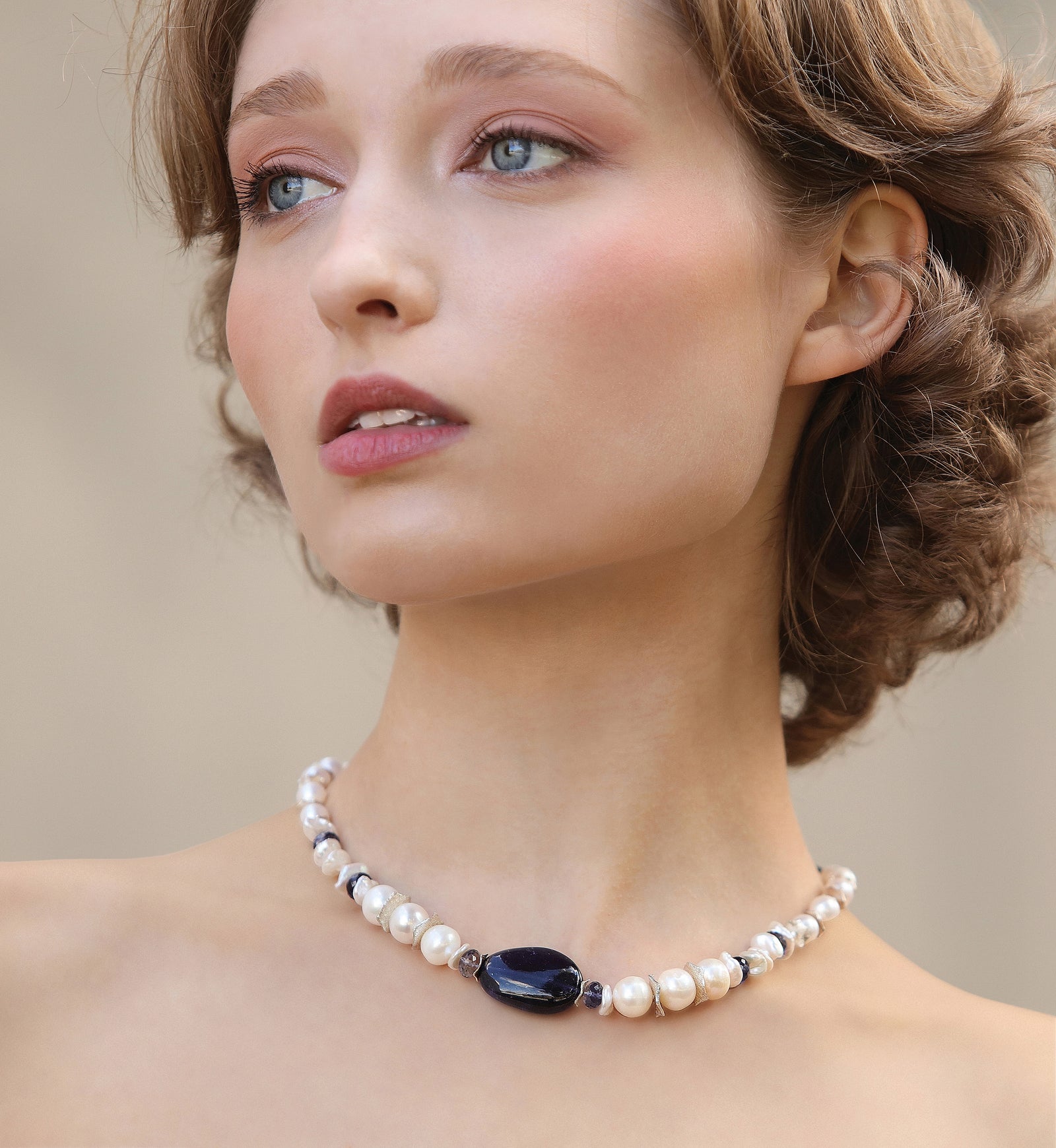 Woman wearing a pearl necklace with a dark stone on a neutral background